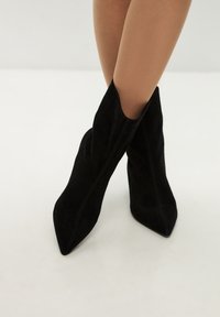 Svarta mocka ankle boots med spetsiga tår och höga stilettklackar, med sidoutskärningar och synliga sömdetaljer.
