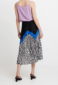 Top viola senza maniche con spalline sottili, abbinato a una gonna nera a pieghe con un motivo a zigzag blu e stampa leopardata bianca.