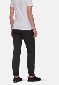 Schwarze Hosen mit taillierter Passform, ausgestattet mit elastischen Bündchen und mehreren Taschen, kombiniert mit schwarzen Sportschuhen mit orangefarbenen Akzenten.