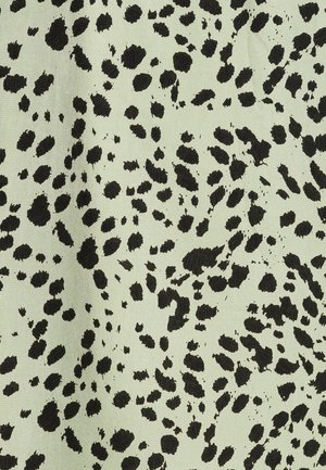 Tela verde claro con una textura que presenta un patrón moteado negro, que recuerda a manchas de animales, dispersas por toda la superficie.