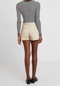 Shorts beiges au texture lisse et avec deux poches arrière, associés à un haut à manches longues rayé noir et blanc. Chaussures noires.