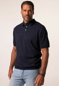 Tummansininen lyhythihainen polo-paita, jossa on kaulus, kolme nappisuljettavaa ja sileä pinta. Yhdistetty vaaleansinihin farkkuihin.