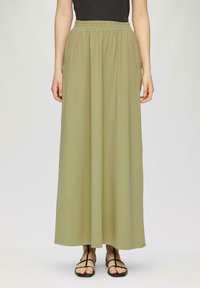 Lange, olijfgroene rok van zacht materiaal met een elastische tailleband, die tot aan de enkels valt. Gepaard met zwarte platte sandaal.