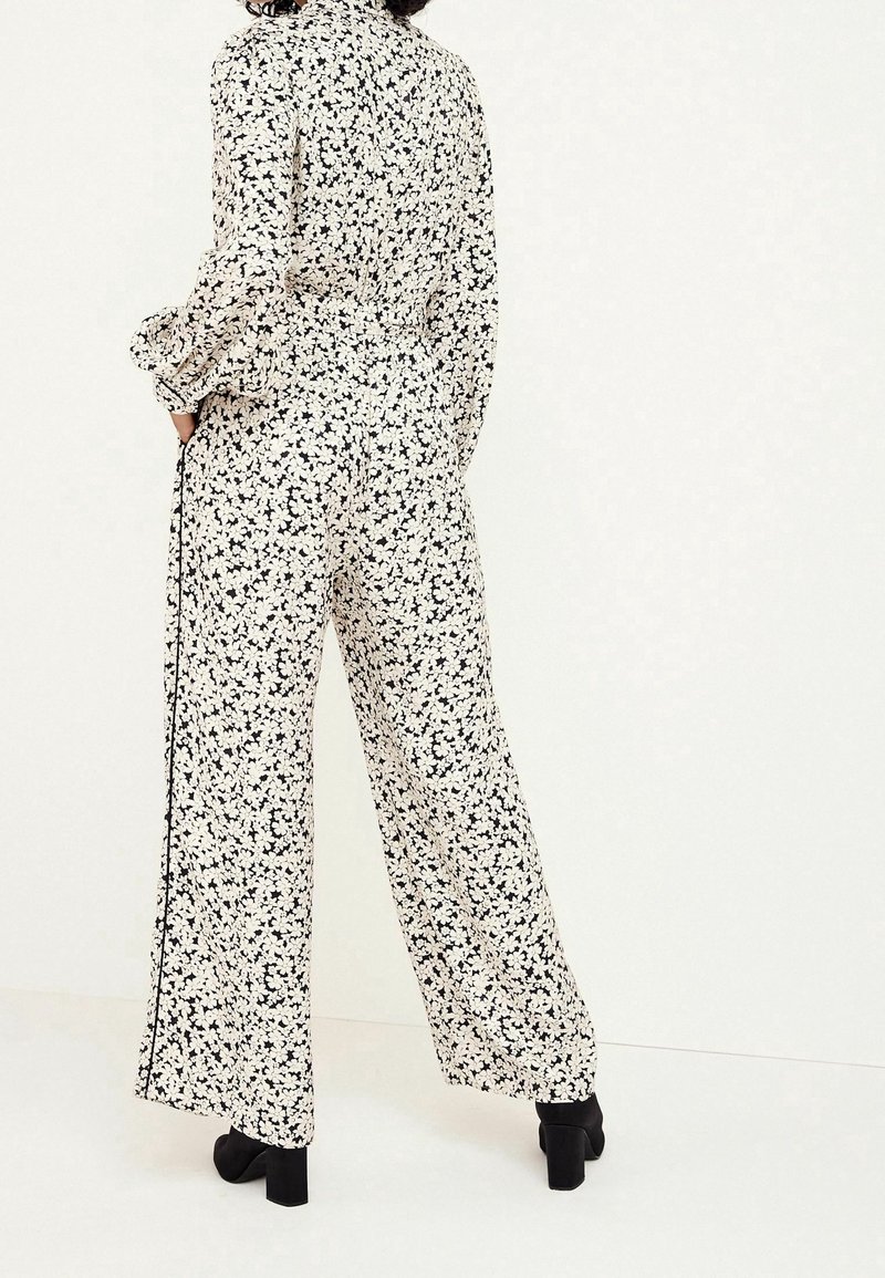 Jumpsuit con motivo floreale in bianco e nero, maniche lunghe, pantaloni a gamba larga, vita aderente e dettagli neri a tinta unita lungo i lati.