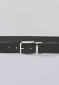 Černý kožený pásek se čtvercovou stříbrnou kovovou přezkou. Má malé otvory pro nastavení velikosti a logo u přezky.