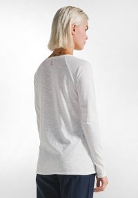 Wit T-shirt met lange mouwen van lichtgewicht, textuurstof met een ronde halslijn en raglanmouwen; heeft een klein roze label aan de achterkant.