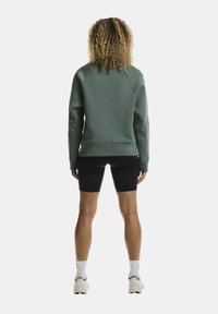 Roheline sviiter ümmarguse kaelusega, soonikute varrukatega ja lõdvema sobivusega, koos mustade rattapükste ja valgete sportlike jalanõudega.