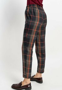 Spodnie w kratę w ciemnych kolorach z czerwonymi, pomarańczowymi i niebieskimi wzorami. Posiadają elastyczny pas i luźny krój.