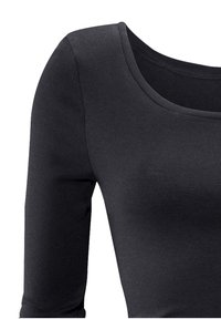 Zwarte, aansluitende longsleeve top gemaakt van soepele, rekbare stof. Heeft een ruime halslijn en een geribbelde textuur langs de mouwen.