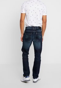 Mörkblå denimjeans med rak ben design, bakfickor och subtila blekningar. Matchas med en vit skjorta med kort ärm som har ett mönster.