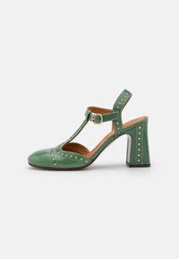 Green patent leather shoe with a T-bar strap, round toe, and block heel. Features decorative perforations along the sides and strap.