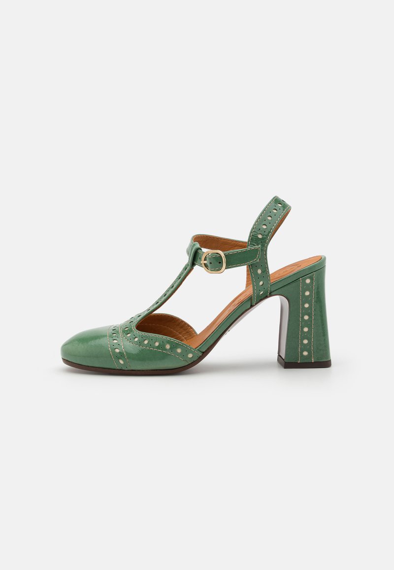 Green patent leather shoe with a T-bar strap, round toe, and block heel. Features decorative perforations along the sides and strap.