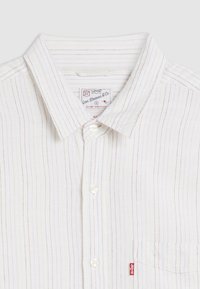 Camicia bianca con bottoni, con sottili righe rosse e blu, colletto classico, taschino singolo sul petto e etichetta del marchio cucita sulla tasca.