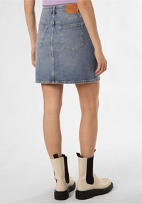 Denim mini hame, joka on vaaleansininen, näkyvillä ompeleilla ja kahdella takataskulla, yhdistettynä beigeihin nilkkureihin, joissa on mustat elastiset osat.