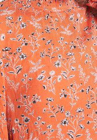 Tissu orange avec un motif délicat de petites tiges florales blanches et noires et feuilles, réparties uniformément sur la surface.