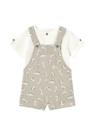 Pantalones de tirantes beige con estampado de dinosaurios, que cuentan con cierres de botón y una camiseta blanca de manga corta debajo. Tela de algodón suave, diseño casual.