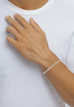Silberarmband mit kleinen Perlen und einem Verschluss, getragen am Handgelenk, neben einem hellfarbenen T-Shirt. Glatte Oberfläche, minimalistisches Design.