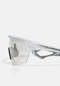 Transparente Sportsonnenbrille mit grauen Gläsern, einem kantigen Design und Gummiakzenten an der Nase und den Schläfen für besseren Halt.