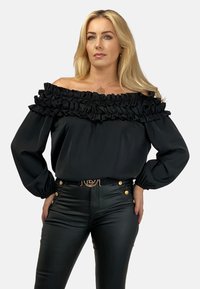 Czarna bluzka bez ramiączek z falbanką przy dekolcie, długimi rękawami i miękkiego materiału. Zestawiona ze świecącymi, dopasowanymi spodniami w kolorze czarnym oraz paskiem z akcentami złota.