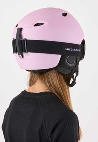 Roze skihes met ventilatiegaten, verstelbare zwarte band en merknaam op de band. Matte afwerking, lichtgewicht ontwerp en gestroomlijnde vorm.