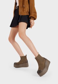 Stivaletti in suede marrone con suola piatta a spessore e pannelli laterali elastici; presentano una punta arrotondata e un tacco basso.