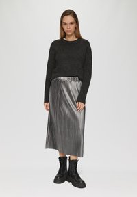 Grijze gebreide trui gecombineerd met een zilveren geplooide midi-rok en zwarte veterschoenen. Soepele texturen en contrasterende kleuren.
