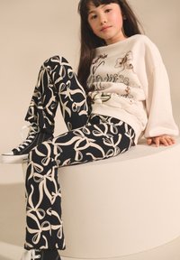 Black and white patterned leggings feature a floral bow design; paired with a light-colored sweatshirt and black high-top sneakers.