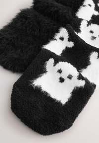 Zwarte, pluizige sokken met witte spookontwerpen. De spoken hebben een pluizige textuur, met zwarte gelaatskenmerken op een zachte witte achtergrond.