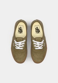 Bruine suède schoenen met witte veters en een gumzool, voorzien van een ronde neus en het Vans-logo aan de binnenkant. Het ontwerp is klassiek en laagprofiel.