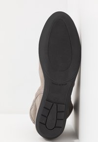 Bottine en daim avec un dessus gris et une semelle en caoutchouc noir texturé, présentant un bout arrondi et des détails de couture visibles. Taille 37, fabriquée en Espagne.
