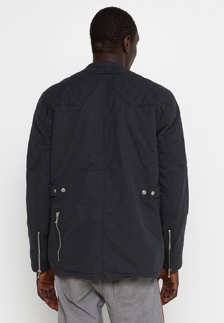 Schwarze gesteppte Jacke mit zwei Reißverschlusstaschen, Druckknopfverschlüssen an der Taille und strukturierten Details an den Schultern.