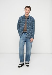 Jachetă din denim albastru cu model, cu guler, două buzunare frontale, asortată cu blugi largi de culoare albastru deschis și pantofi alb-negru.