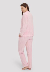Conjunto de pijama rosa que incluye mangas largas y pantalones largos, hecho de una tela suave con un pequeño patrón de corazones blancos en toda su superficie.
