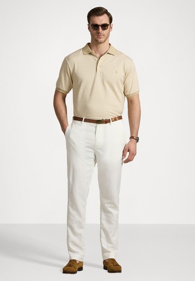 Beige polo shirt met subtiel patroon, witte linnen broeken, bruine leren riem en bruine loafers, gecombineerd met donkere zonnebril.