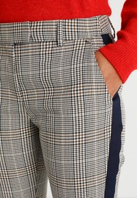 Randiga byxor i grått, vitt och brunt med rak skärning. Har en marinblå sidremsa och sidofickor. Texturerad tyg.