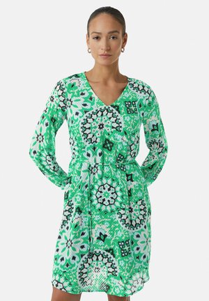 Robe fleurie verte avec des manches longues, un décolleté en V et une taille cintrée. Présente des motifs abstraits dans différentes nuances de vert, noir et blanc.