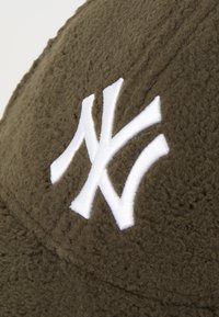 Boné castanho texturizado com logotipo "NY" bordado em branco. Material macio, semelhante a veludo, com costura distinta e aba curva.