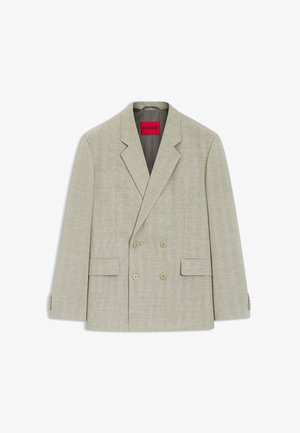 Lichtbeige dubbelgeknoopt jasje met inkeping-revers, vier knopen aan de voorkant, twee klepzakken en een zichtbaar rood "HUGO" label aan de binnenkant van de kraag.