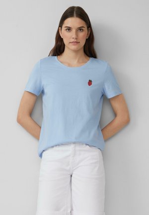 T-shirt en coton bleu clair avec des manches courtes, un col rond et un détail de fraise rouge brodé sur le côté gauche de la poitrine.