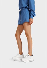 Sneaker bianchi con accenti grigi, suola spessa e chiusura con lacci. Indossate con una felpa blu e pantaloni corti blu coordinati.