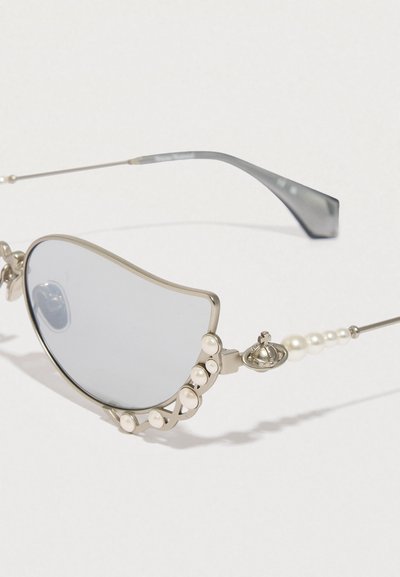 Óculos de sol prateados com lentes em forma de onda únicas e detalhes em pérolas na armação. Apresentam hastes finas e um detalhe decorativo em metal.
