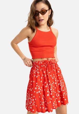Rood geribd crop top met golfrandjes, gecombineerd met een vloeiende rode rok met witte bloemmotieven en een elastische tailleband.
