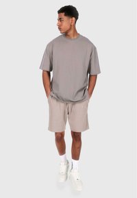 Grå bomulls t-skjorte med avslappet passform, kombinert med beige ribbestrikkede shorts. Modellen har på seg hvite sneakers og ankelsokker.