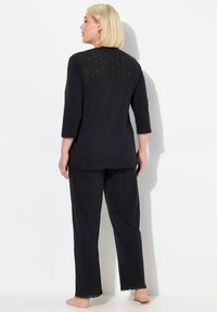 Conjunto de loungewear negro con una blusa de manga tres cuartos que presenta una parte trasera de encaje estampada y pantalones a juego con un dobladillo con puntilla.