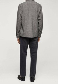 Camisa a cuadros en blanco y negro con cuello extendido y mangas largas, combinada con pantalones de mezclilla oscuros y zapatos negros, vista desde la parte de atrás.