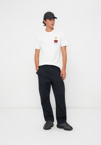 Hvit bomull t-skjorte med grafikk av en rød rose og en krone; paret med svarte cargo-bukser og mørke sneakers; brukt med en svart caps.