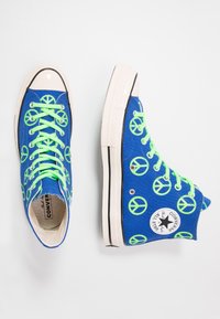 Blue high-top Converse sneakers with neon green peace sign patterns and matching neon green laces, shown from top and side views.