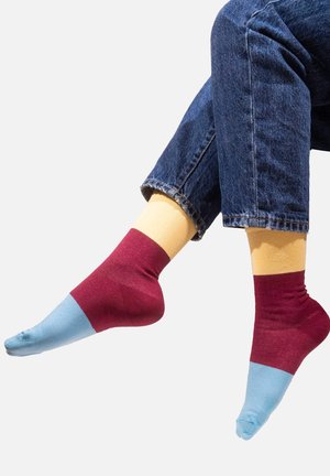 Wielokolorowe skarpetki: bordowe powyżej kostki, żółte na górze i jasnoniebieskie na palcach. Gładki materiał z kontrastowymi blokami kolorów.