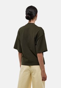 T-shirt oversize vert olive en coton doux, avec un col rond et des manches courtes, associé à un pantalon large jaune clair.