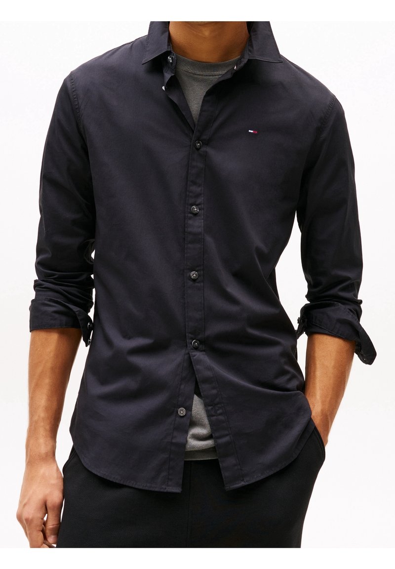 Camisa abotonada en algodón azul marino oscuro, con cuello clásico y mangas remangadas. Destaca el logo en el pecho izquierdo y su textura suave.